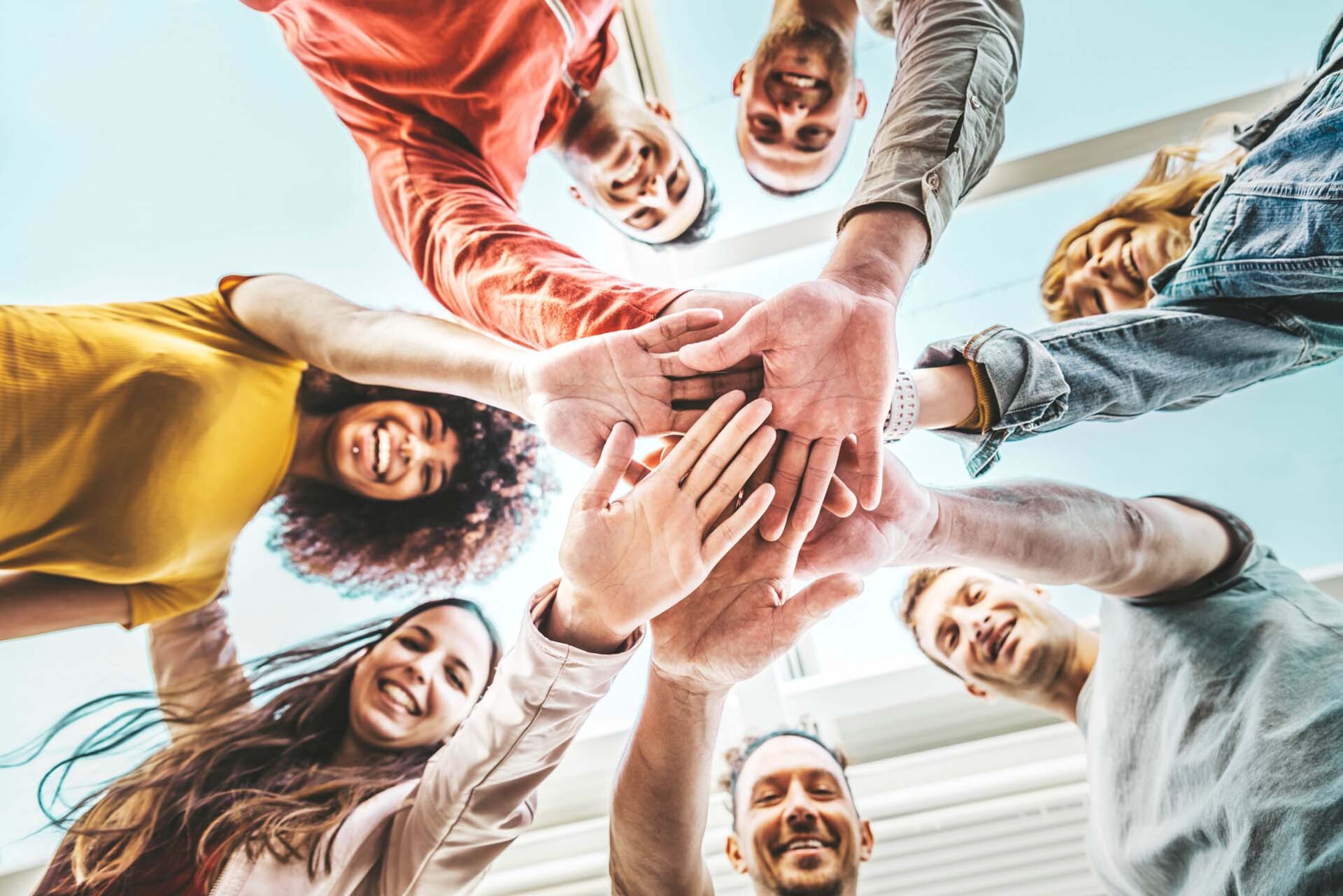 Eine vielfältige Gruppe von Händen, die aus unterschiedlichen Winkeln zusammenkommen und vor einem hellen Hintergrund Einheit und Teamwork symbolisieren.