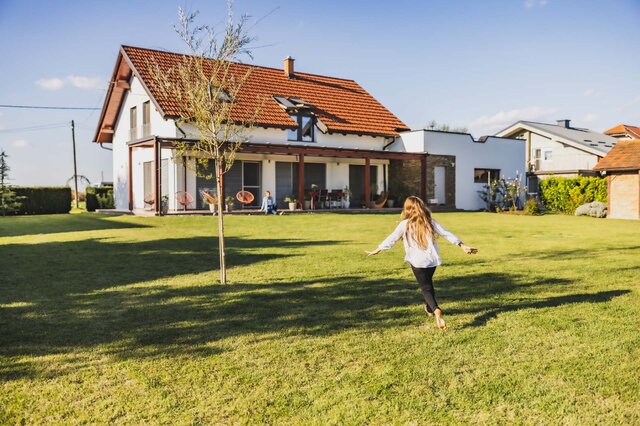 Ein Mädchen läuft Barfuß durch den Garten eines Einfamilienhauses.