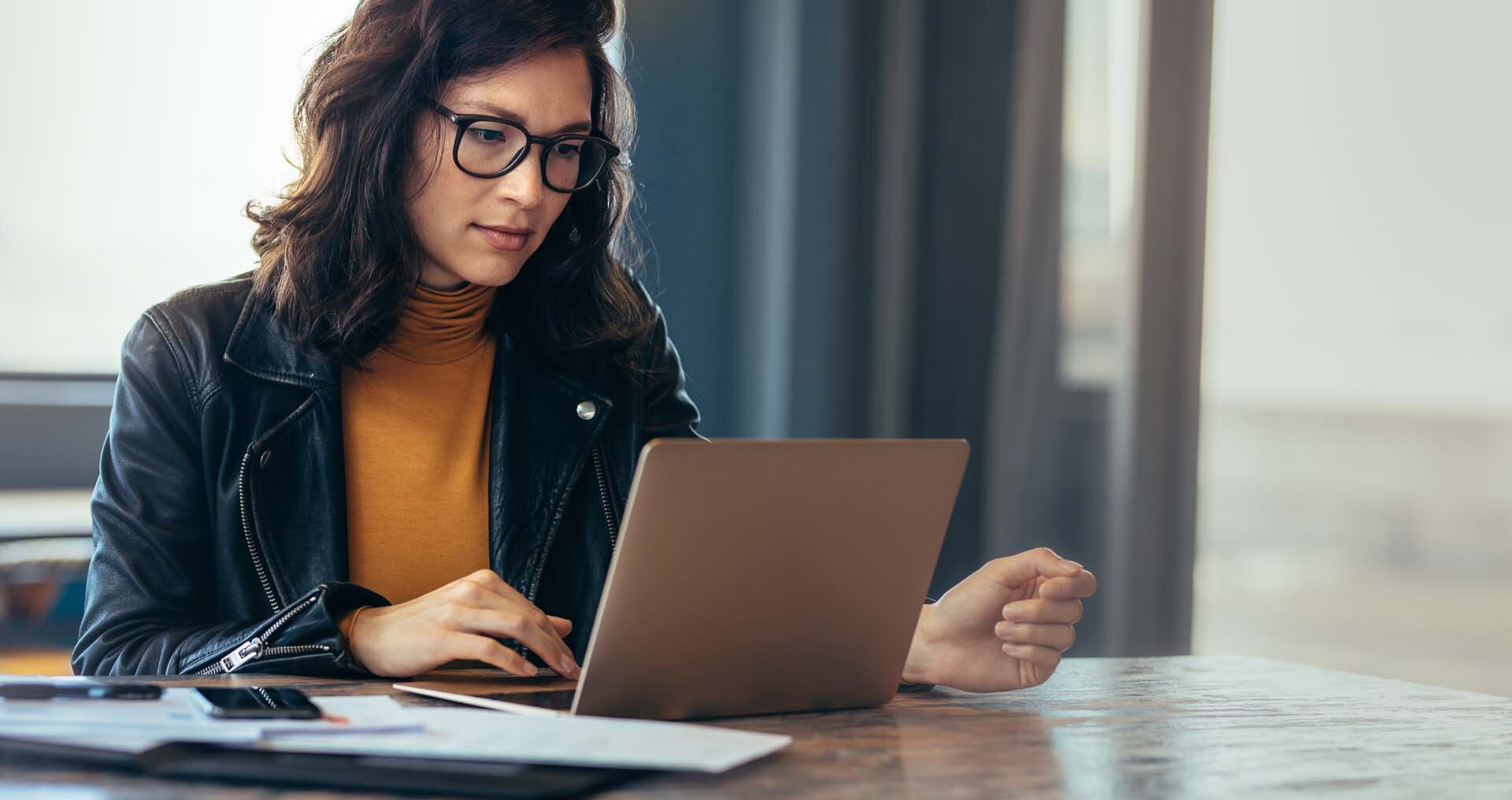 Eine Frau, die eine Brille trägt, arbeitet an ihrem Laptop.