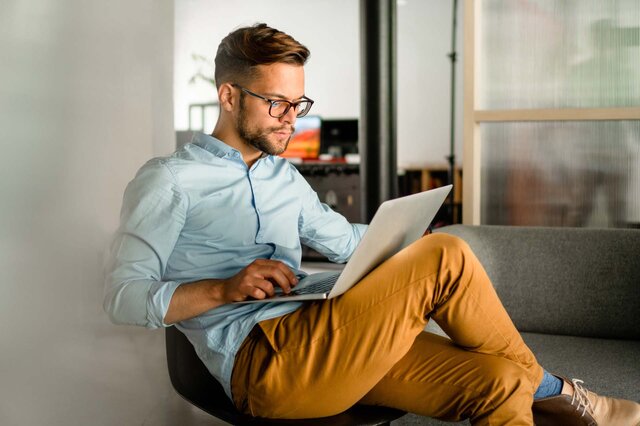 Ein Mann sitzt auf einem Stuhl und arbeitet an seinem Laptop.