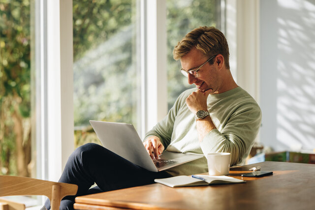 Ein Mann sitzt an einem Tisch und arbeitet an einem Laptop.