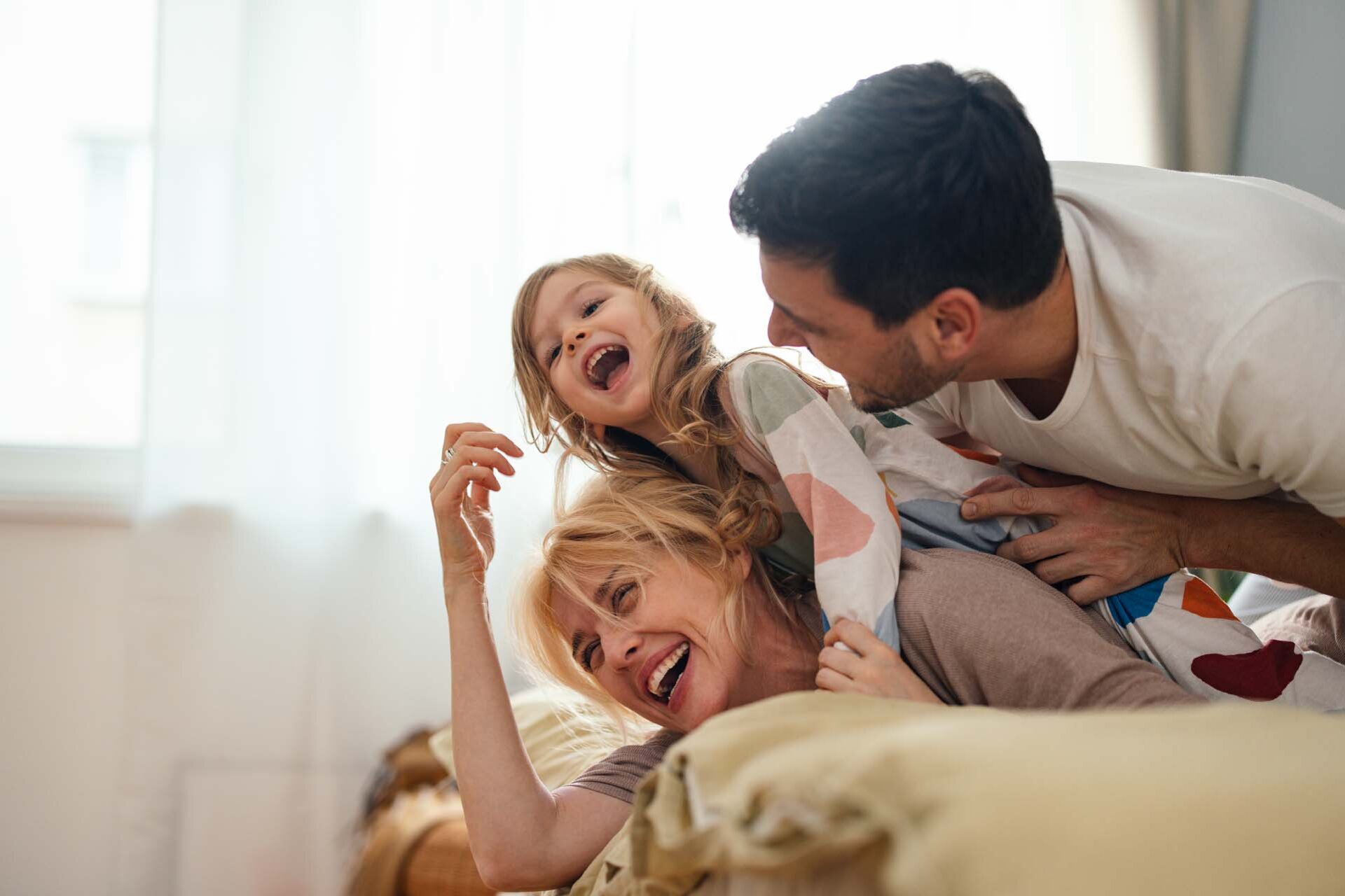 Eine junge Familie tobt lachend auf einem Bett herum.