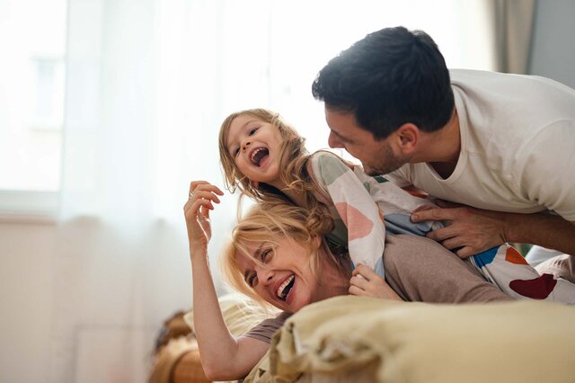 Eine junge Familie tobt lachend auf einem Bett herum.