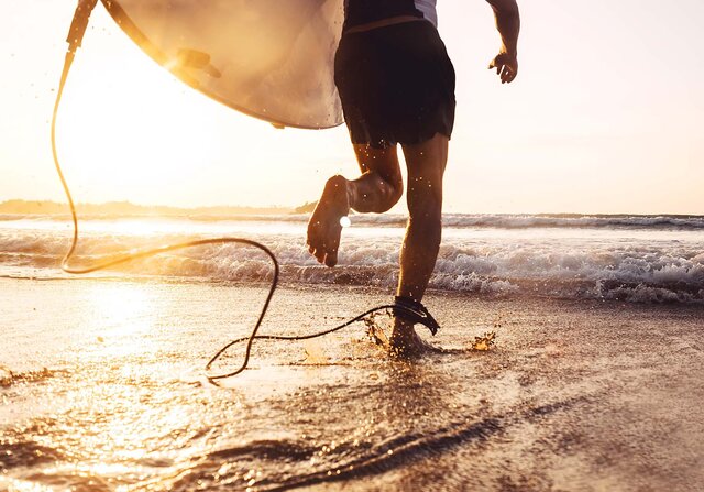 Ein Mann läuft mit einem Surfbrett über den Strand in Richtung Meer.
