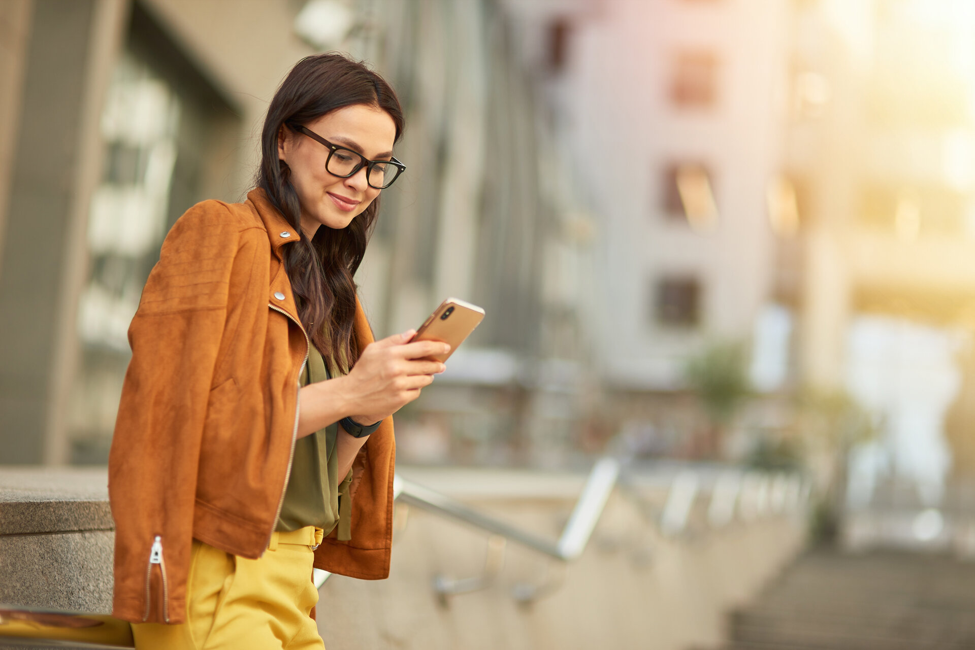 Eine junge Frau mit Brille schaut schmunzelnd auf ihr Handy.
