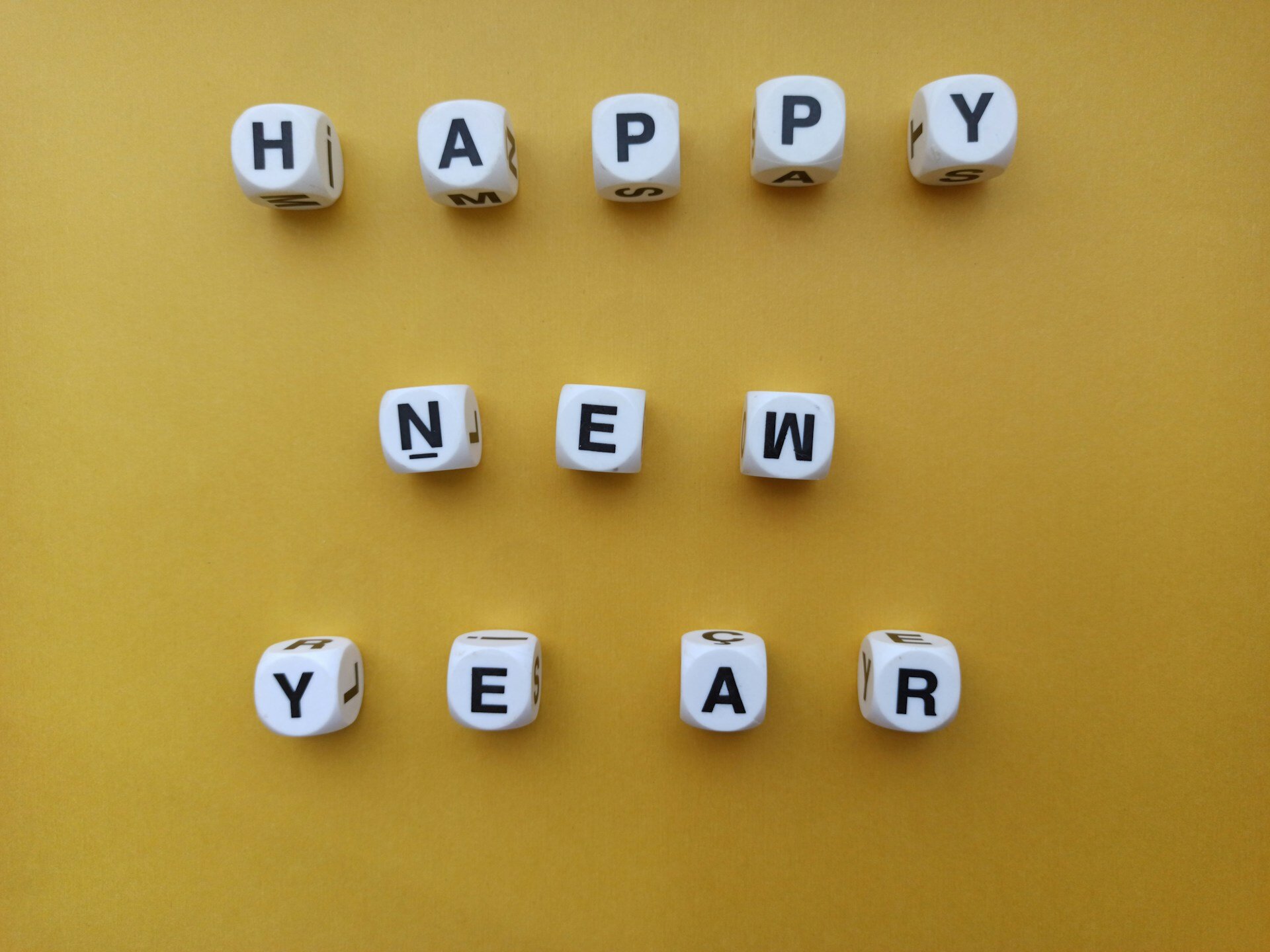 Versicherungen überdenken: Bedarf prüfen und optimieren | © Özgür Öztürk / Unsplash Auf dem Bild sieht man Würfel, die neben- und untereinander das Wort "Happy New Year" ergeben. Der Hintergrund ist gelb. | © Özgür Öztürk / Unsplash