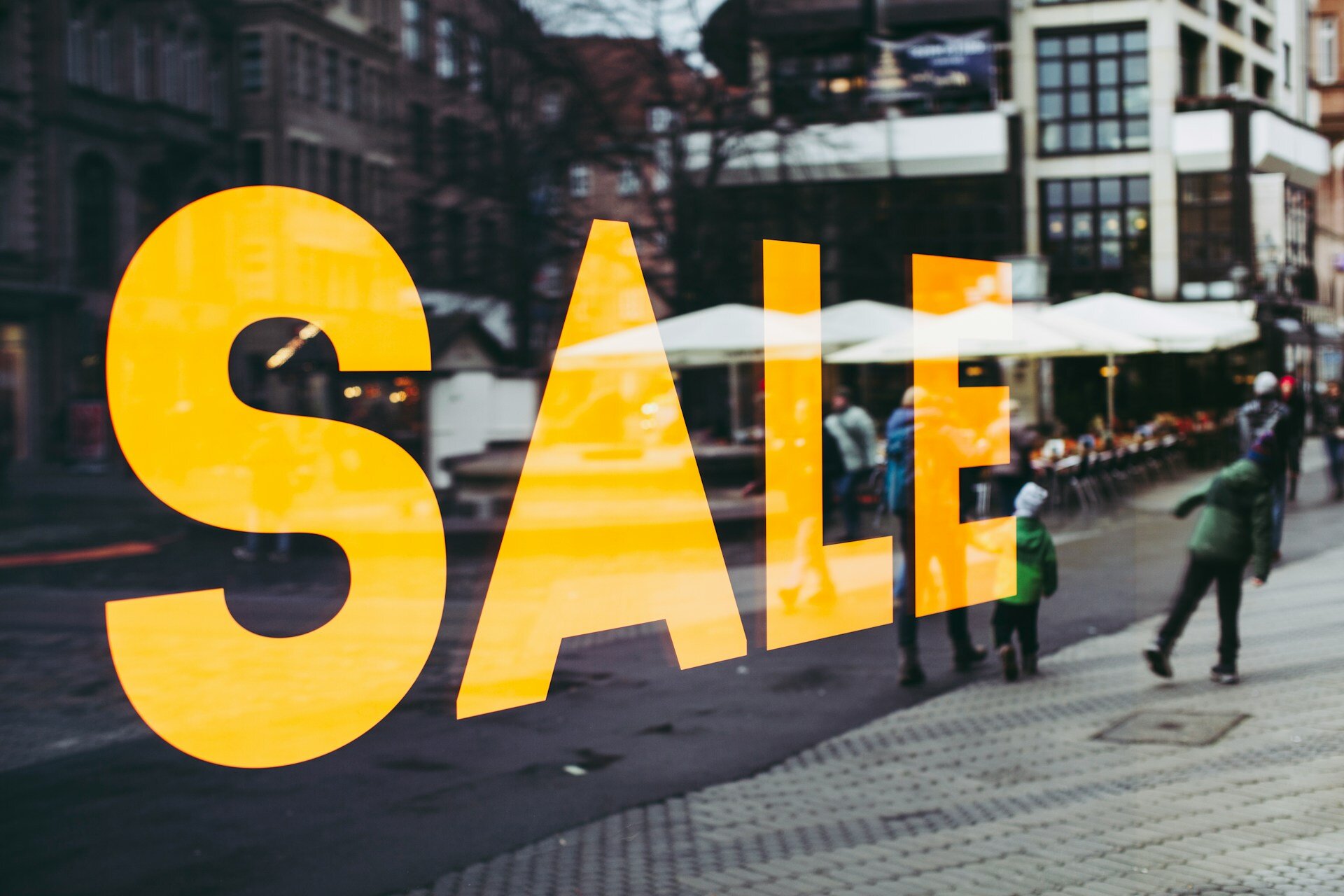 In der reflektierenden Scheibe eines Schaufensters ist das Stadtgeschehen und das Wort "Sale" zu sehen. | © Markus Spiske / Unsplash