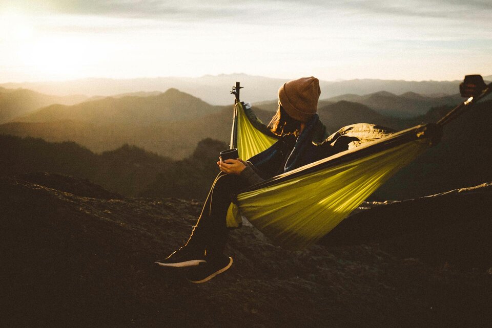 Eine Person sitzt in einer Hängematte auf einem Berggipfel und genießt die Aussicht auf die umliegende Landschaft. | © Dziana Hasanbekava / Pexels