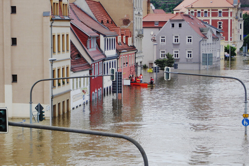 Auf dem Bild sieht man Häuser, die im Hochwasser stehen. Im Hintergrund erkennt man ein Rettungsboot an einem Haus. | © LucyKaef / Pixabay