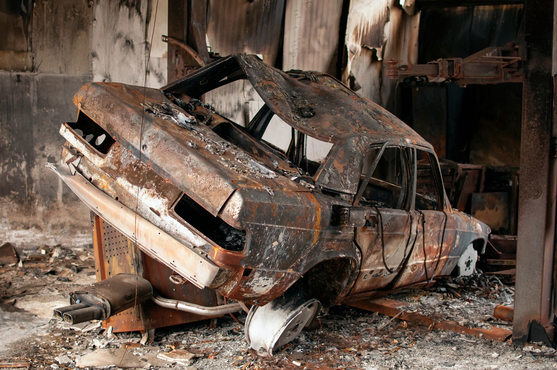 Kfz-Versicherung: Wer zahlt nach Werkstattbrand? | © Harry Dona / unsplash Auf dem Bild ist ein ausgebranntes Autowrack zu sehen, das in einer Werkstatt steht. | © Harry Dona / unsplash