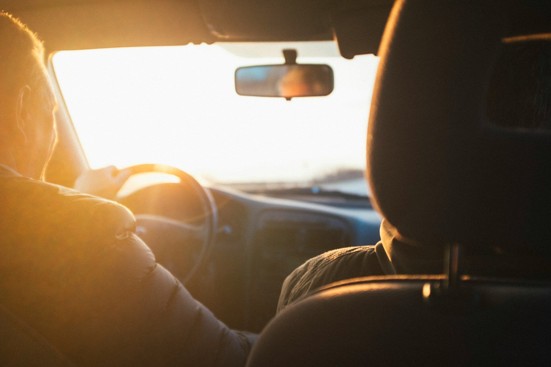 Zwei Personen im Auto, das bei Sonnenuntergang fährt, während der Himmel in warmen Tönen erstrahlt. | © Darwin Vegher / Unsplash