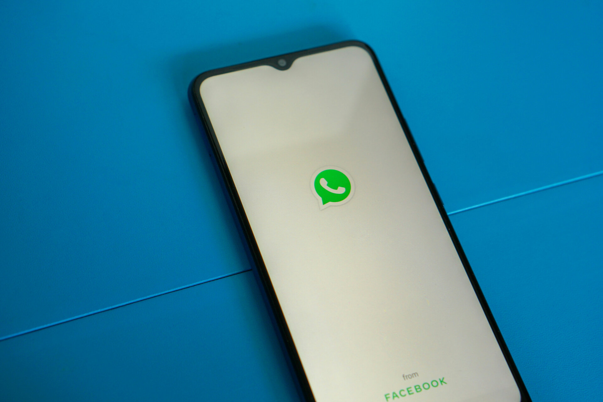 Versicherung per WhatsApp? Sinnvoll oder nur trendy? | © Mourizal Zativa/Unsplash Das Bild zeigt ein Smartphone, auf dem das WhatsApp-Logo zu sehen ist, vor blauem Hintergrund | © Mourizal Zativa/Unsplash