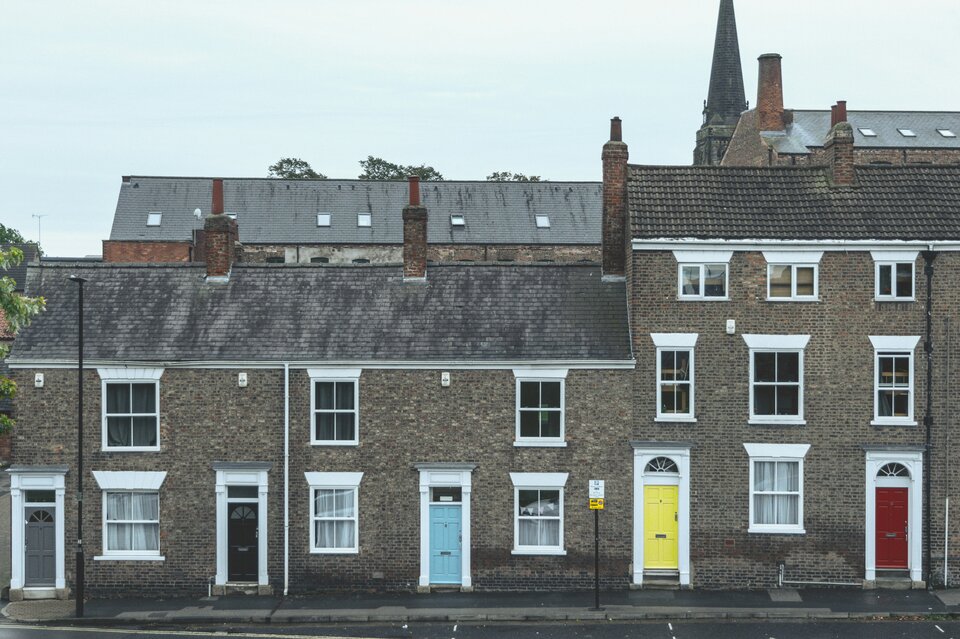 Versicherungen für Wohnungseigentümer: Was Sie wissen müssen | © Gonzalo Facello/Unsplash Auf dem Bild sieht man eine Häuserreihe mit farbigen Eingangstüren | © Gonzalo Facello/Unsplash