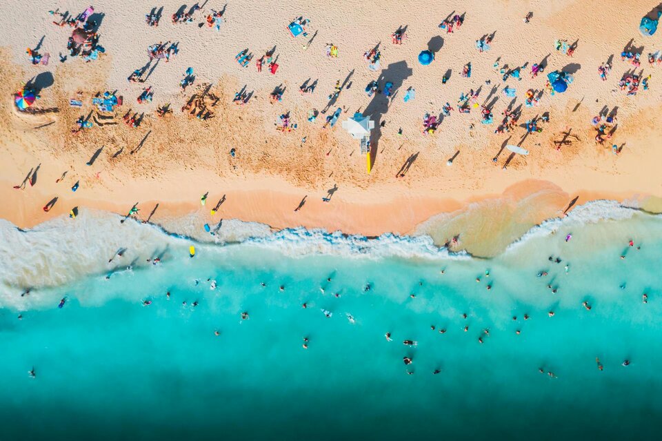 Das Bild zeigt einen Strand mit Menschen von oben. | © Jess Loiterton / Pexels