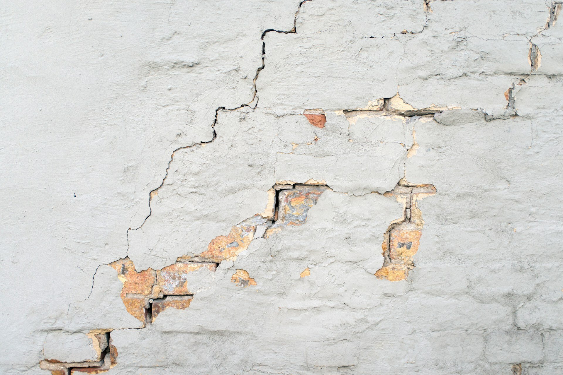 BGH-Urteil: Differenzierung zwischen Erdrutsch und Erdkriechen | © Oleg Stepanov / Unsplash Auf dem Bild sieht man eine Wand mit mehreren Rissen, zudem löst sich der weiße Farbe an einigen Stellen. | © Oleg Stepanov / Unsplash