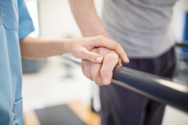Eine medizinische Fachkraft hält sanft die Hand eines Patienten.